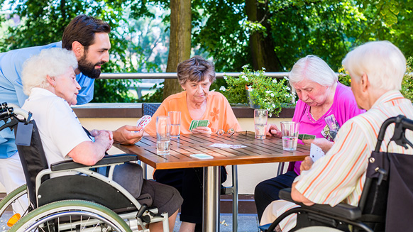 Pfleger mit Seniorinnen beim Kartenspielen | Quelle: © Kzenon / Adobe Stock