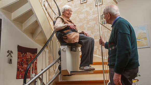 Älteres Paar auf der Treppe mit Treppenlift | Quelle: © Ingo Bartussek / Adobe Stock