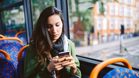 Frau in Bus schaut aufs Handy | Quelle: © lechatnoir via Getty Images